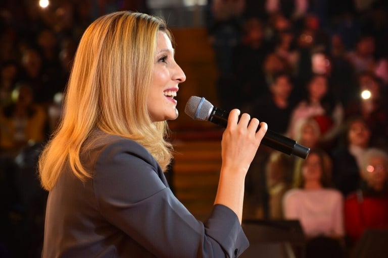 Woman speaking into microphone on stage with audience in background